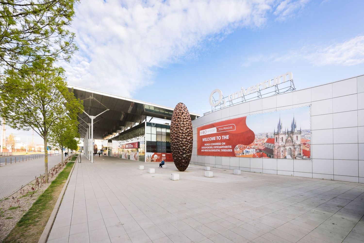Modern convention center exterior with a Welcome to Prague banner and sculpture outside.