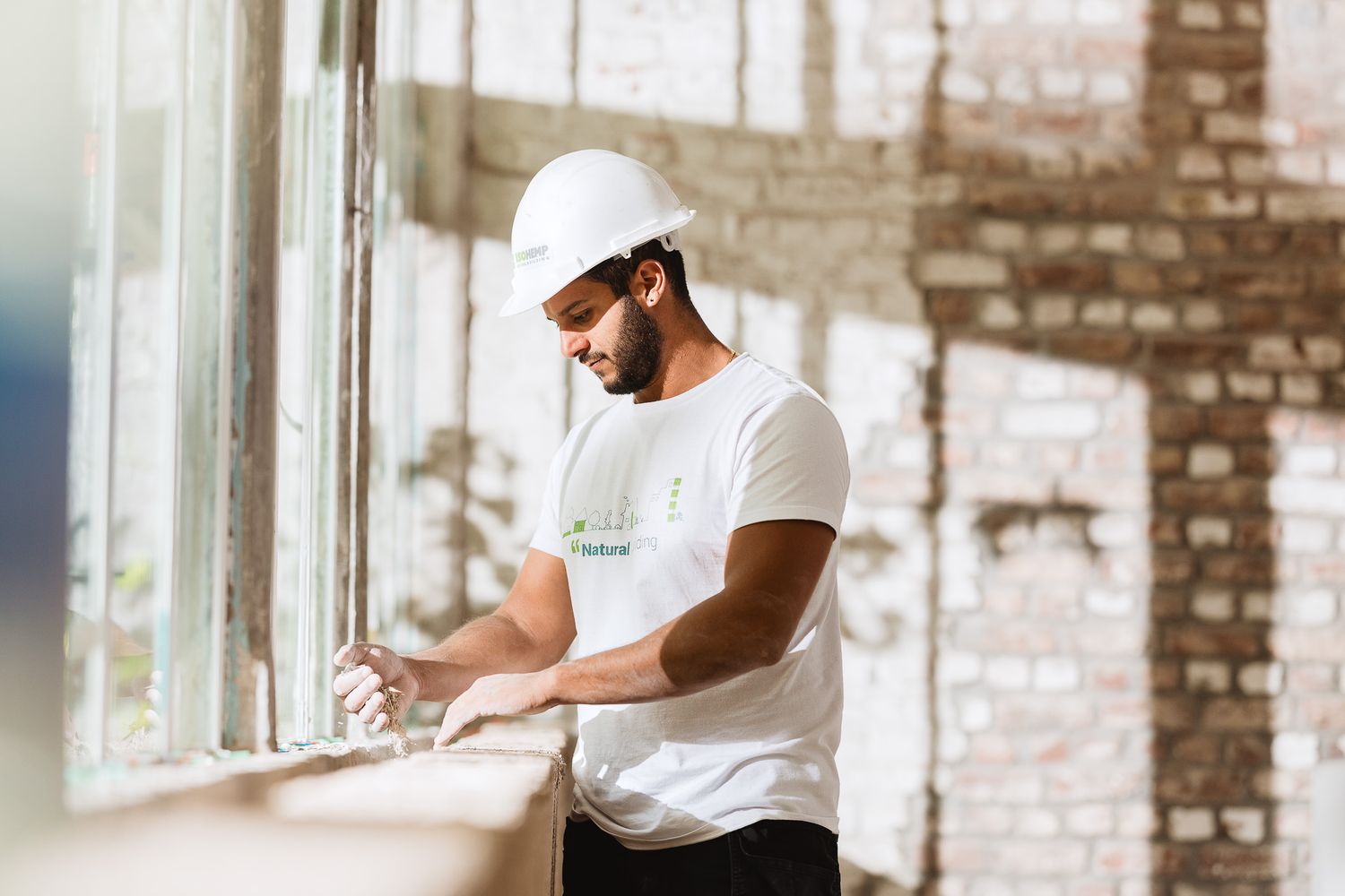 Construction worker in white hard hat working on a window ledge in a brick building.