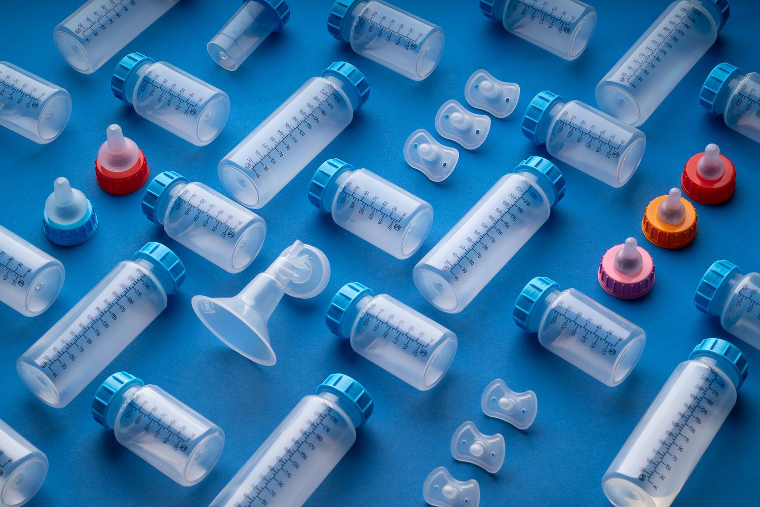 Multiple clear plastic baby bottles with blue caps and colorful pacifiers on blue background.