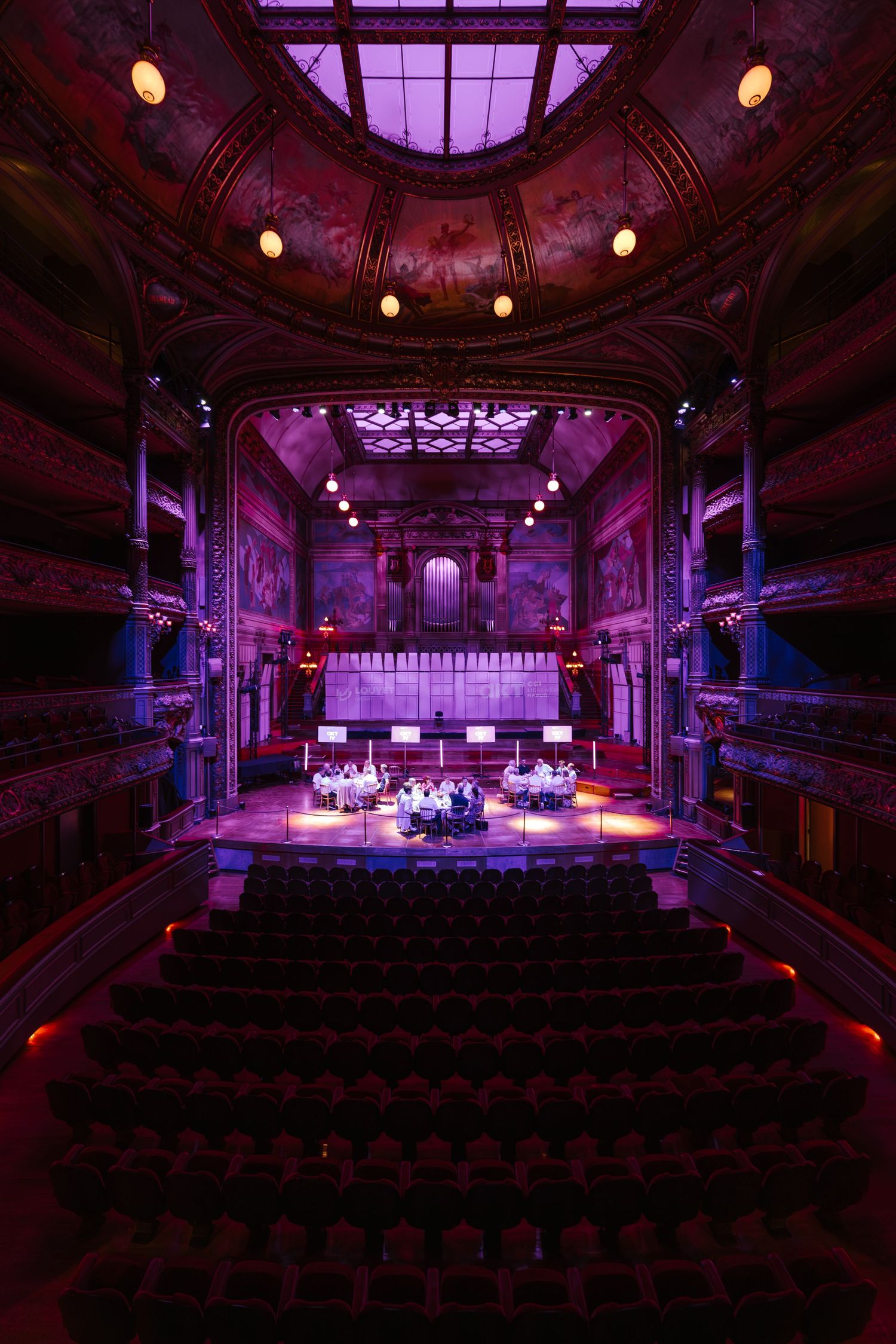 Stunning vintage theater with purple lighting, ornate balconies, painted ceiling, and musicians performing on stage.