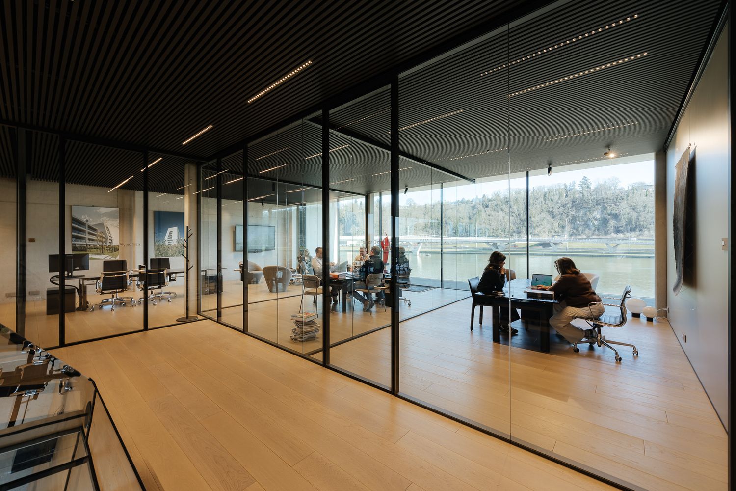 Modern office with glass partition walls, open workspace, and panoramic views of green landscape.