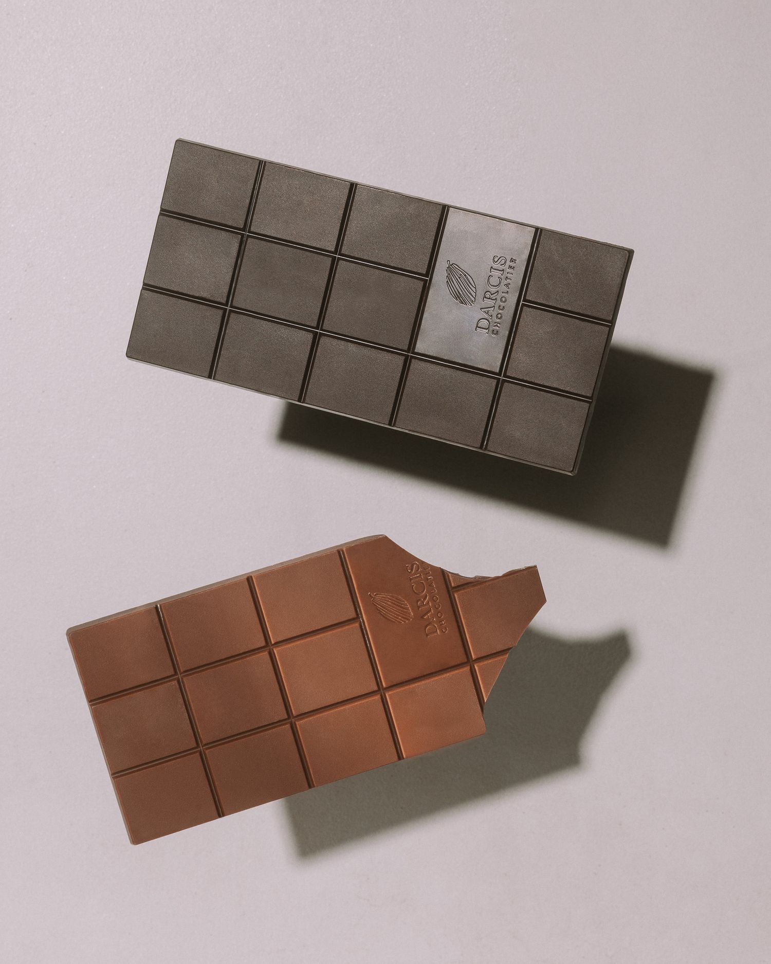 Two chocolate bars, one dark and one milk chocolate, displayed on a light background.
