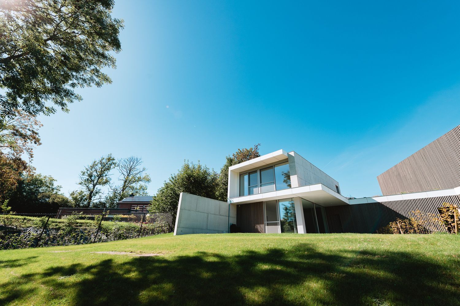 Contemporary white villa with flat roof, large windows, and lush green garden under blue sky.