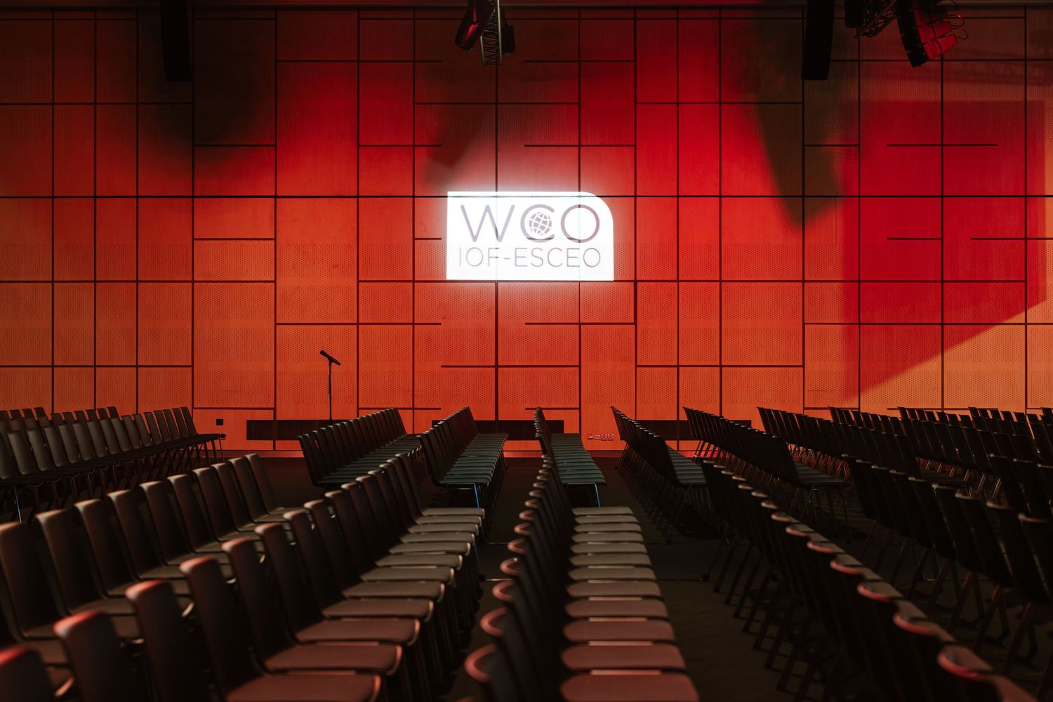 Empty red-lit auditorium with rows of seats facing a glowing WCO Prague screen.