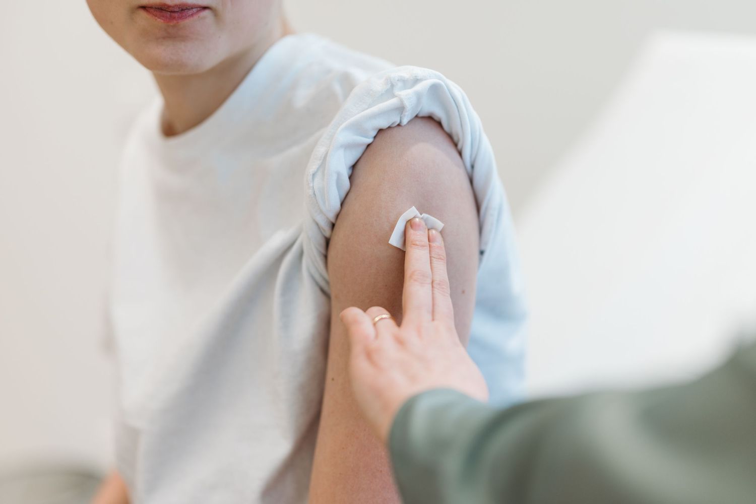 Healthcare worker applying a cotton swab to a child's arm after vaccination in a medical setting.