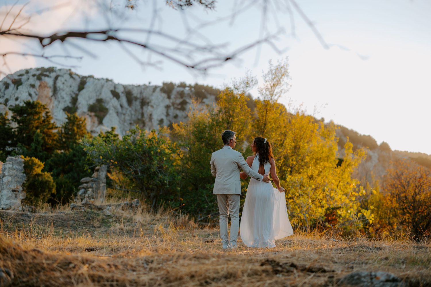 Bride and groom holding hands walking through a scenic rocky landscape at golden hour sunset.