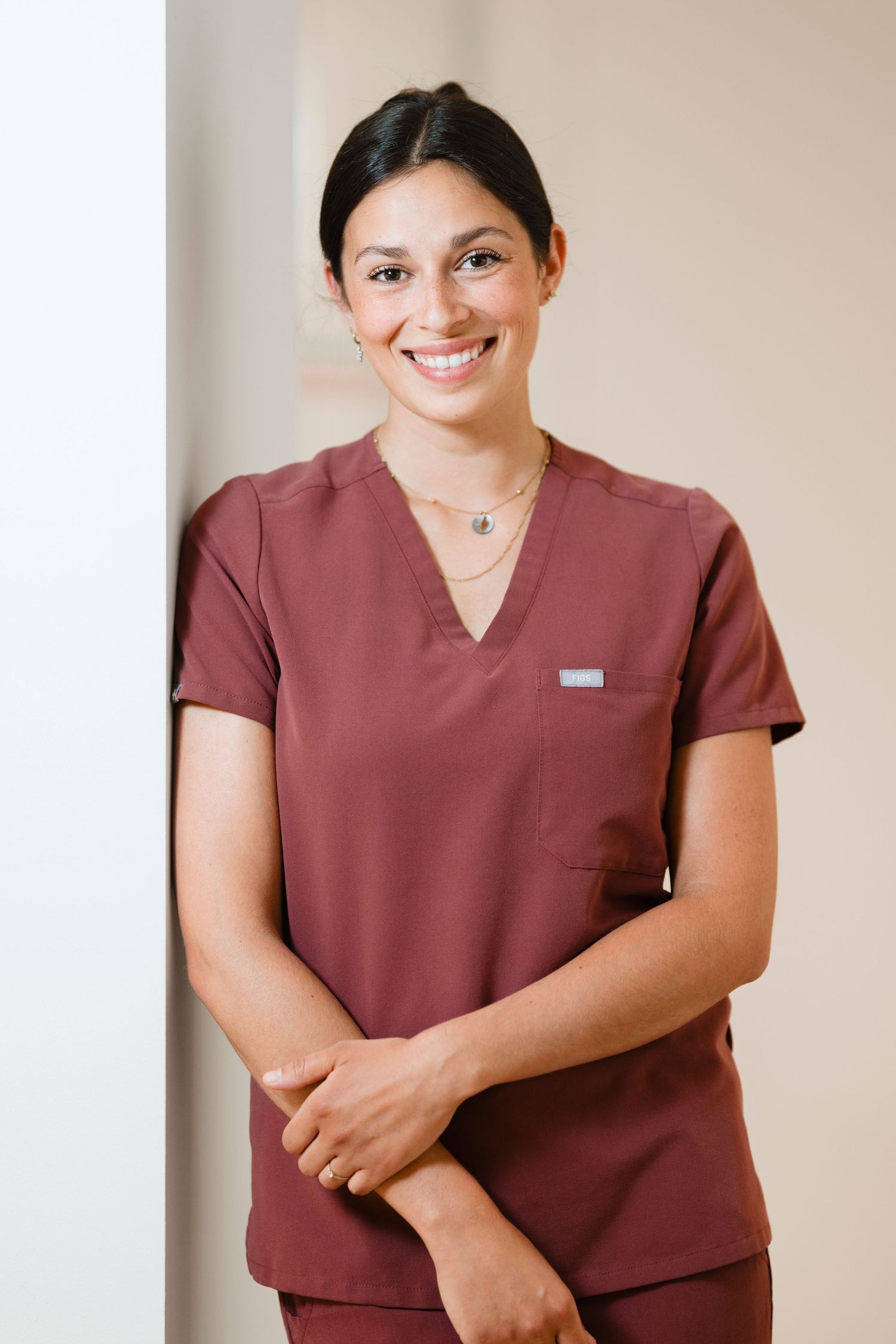 Smiling female healthcare professional in maroon scrubs posing confidently in a medical facility.