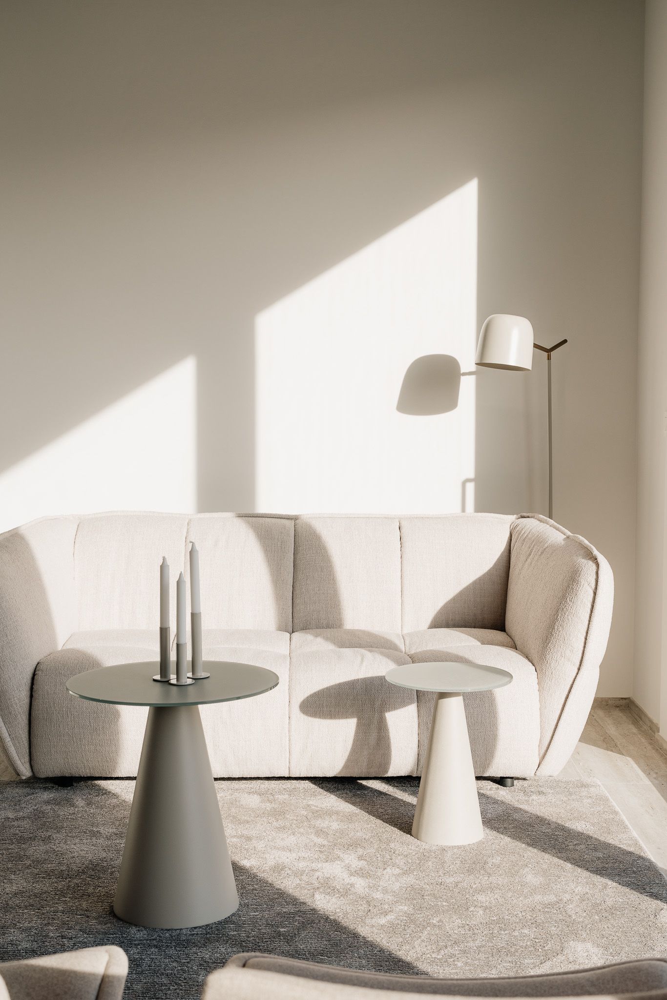 Minimalist living room with curved cream sofa, round side tables, floor lamp, and natural sunlight casting shadows.