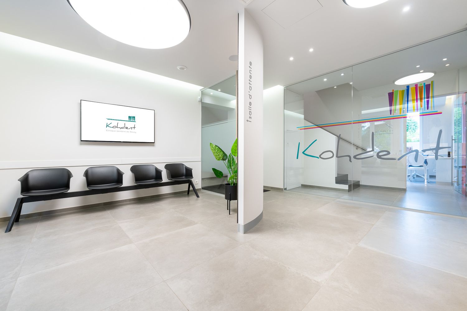 Modern dental clinic waiting room with black seating, a display screen, and Koncert branding on glass wall.