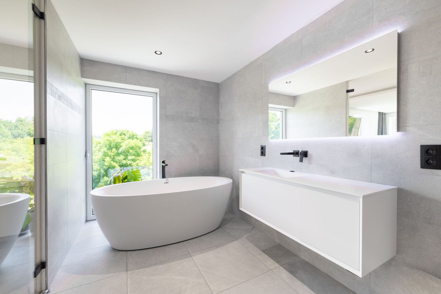 Modern minimalist bathroom featuring a freestanding white soaking tub, floating vanity, and large window with garden view.