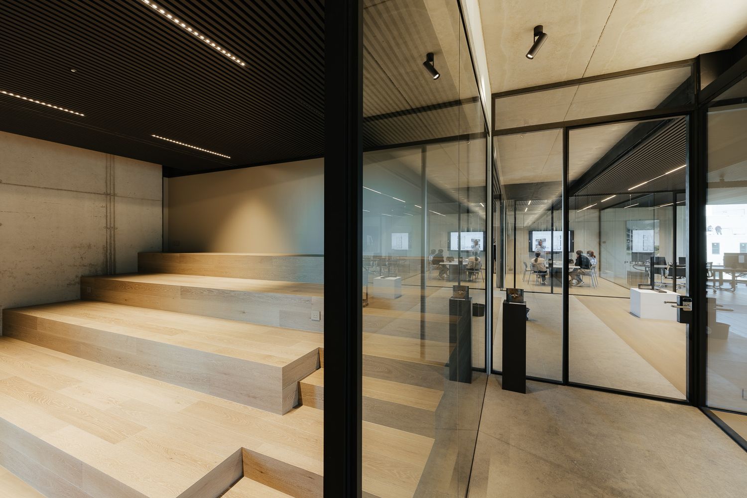 Contemporary office interior featuring wooden stairs, glass partition walls, and open workspace beyond.