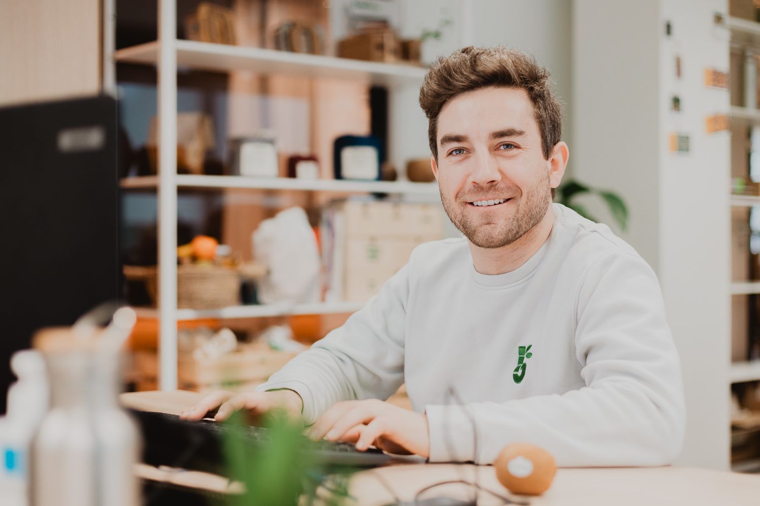Smiling young man in a grey sweatshirt sitting at a counter in a modern cafe.
