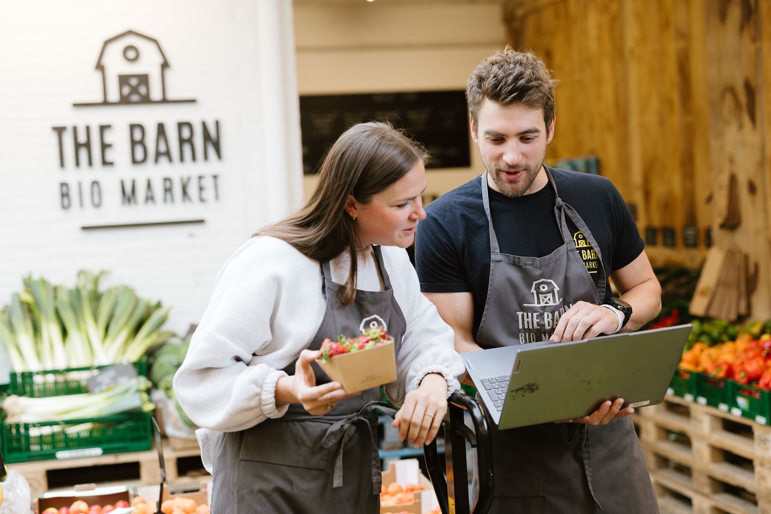 Two employees in aprons reviewing data on a laptop at The Barn Bio Market.