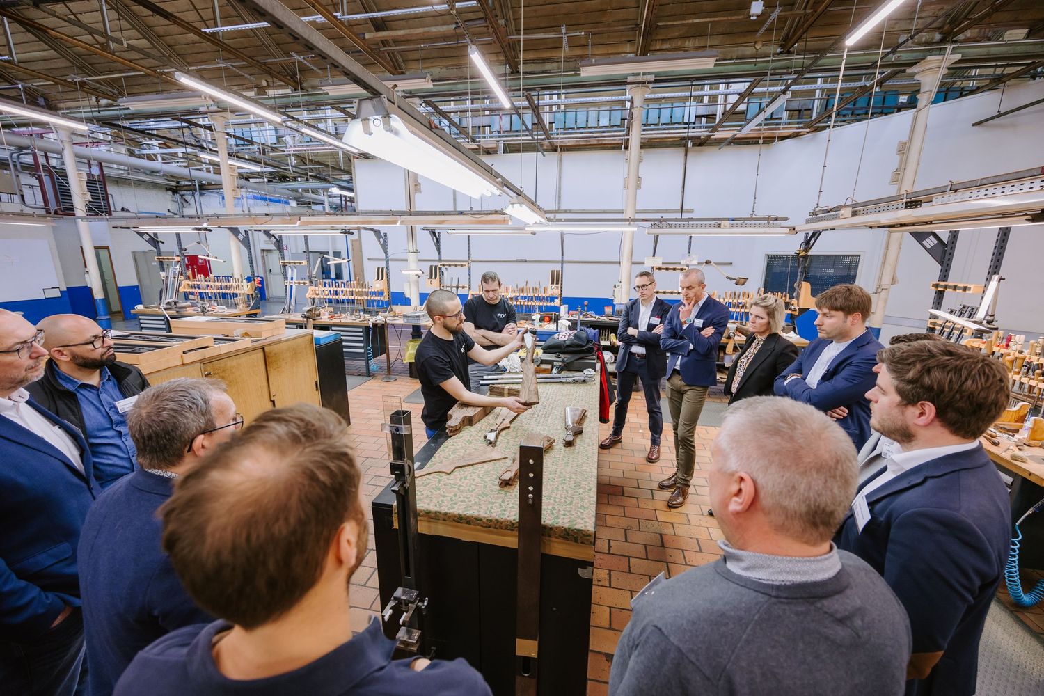 Group of professionals observing manufacturing demonstration in industrial workshop facility.