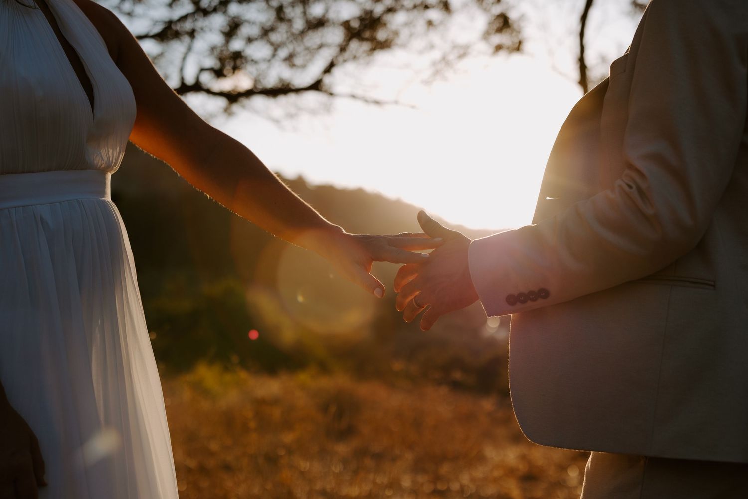 Couple holding hands at golden sunset with warm lens flare during an outdoor engagement session.