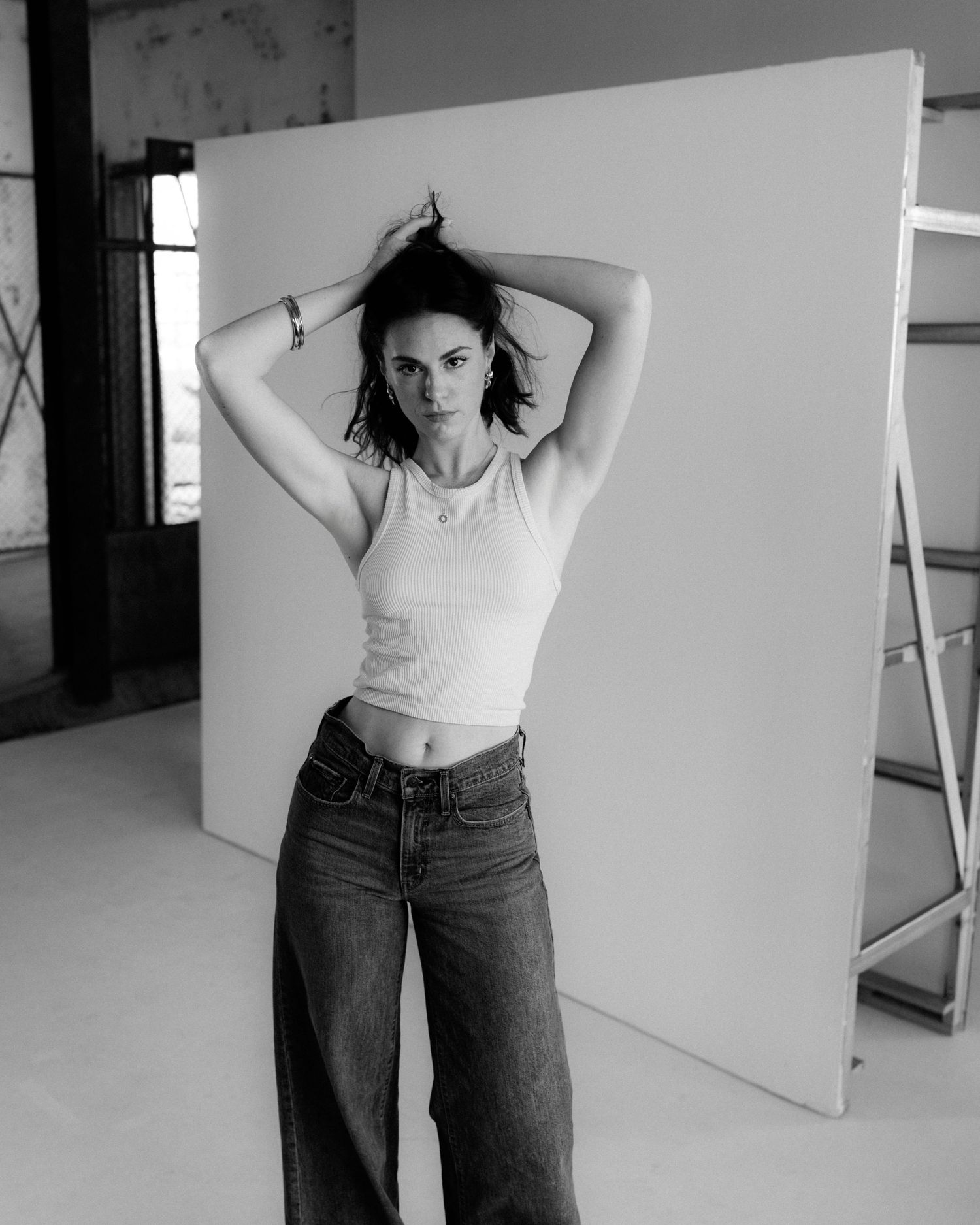 Black and white portrait of a young woman in crop top and wide-leg jeans posing in a photography studio.