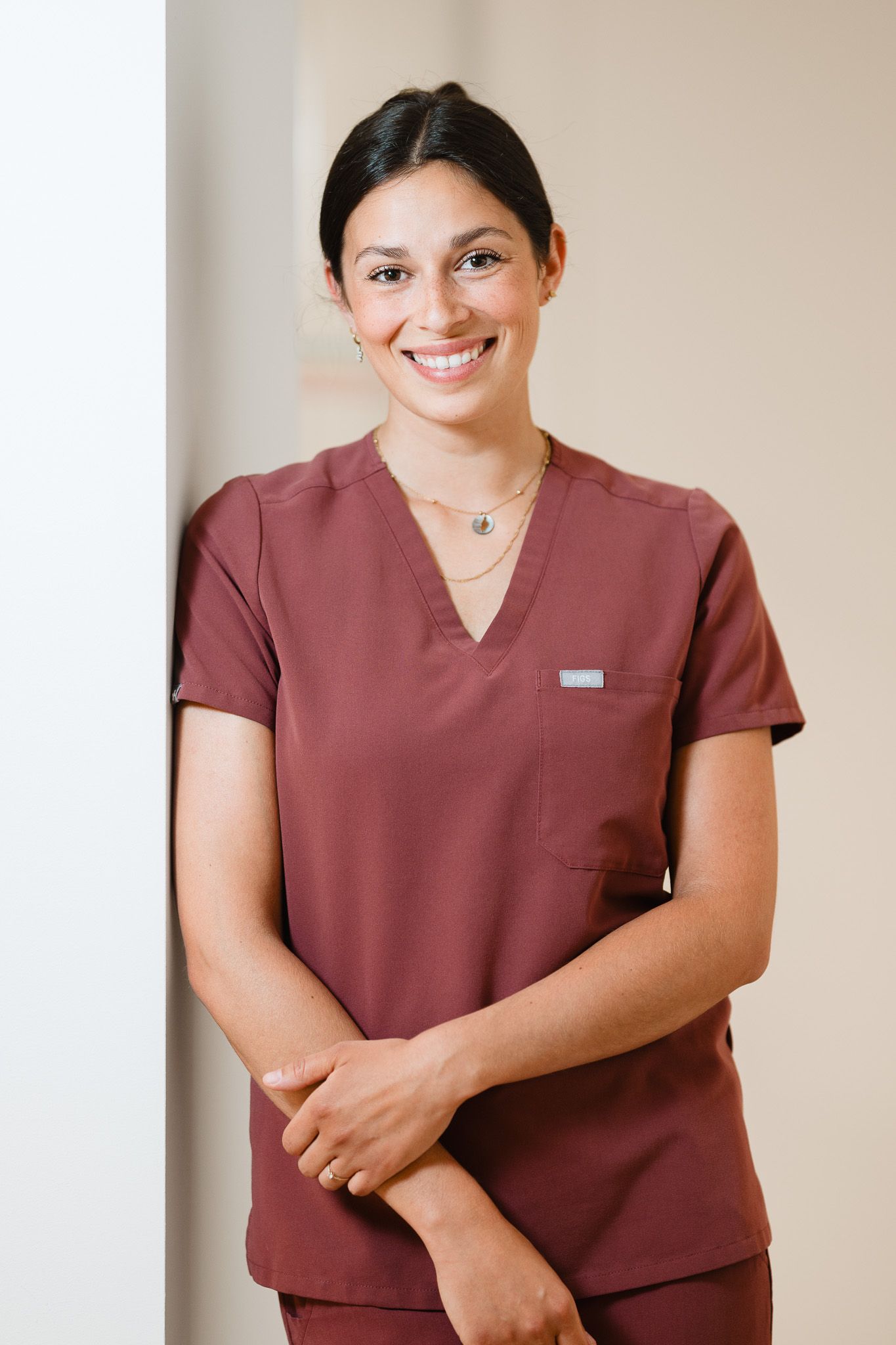 Smiling female healthcare professional in maroon scrubs posing in a medical office.
