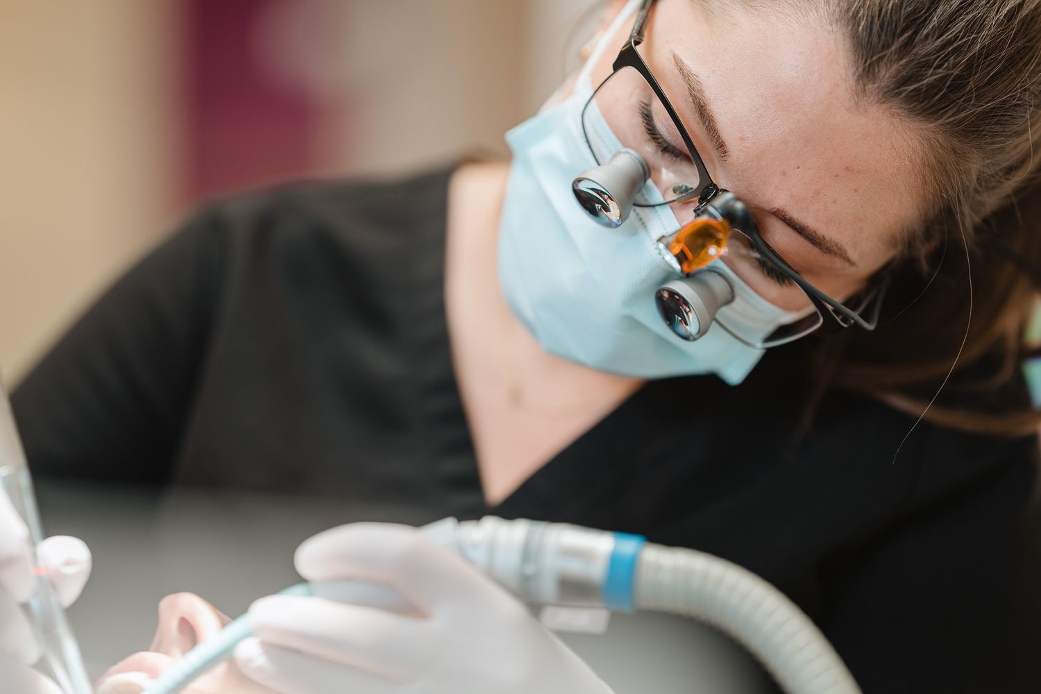 Female dentist wearing magnifying loupes and surgical mask performing a precise dental procedure on a patient.