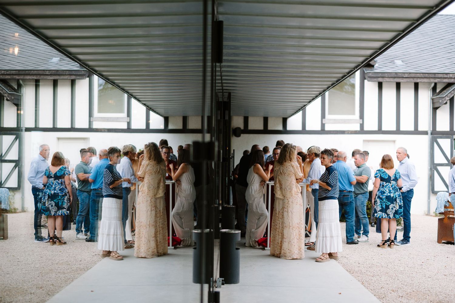 Guests mingling at an outdoor wedding reception, reflected in a mirror, creating a symmetrical effect.