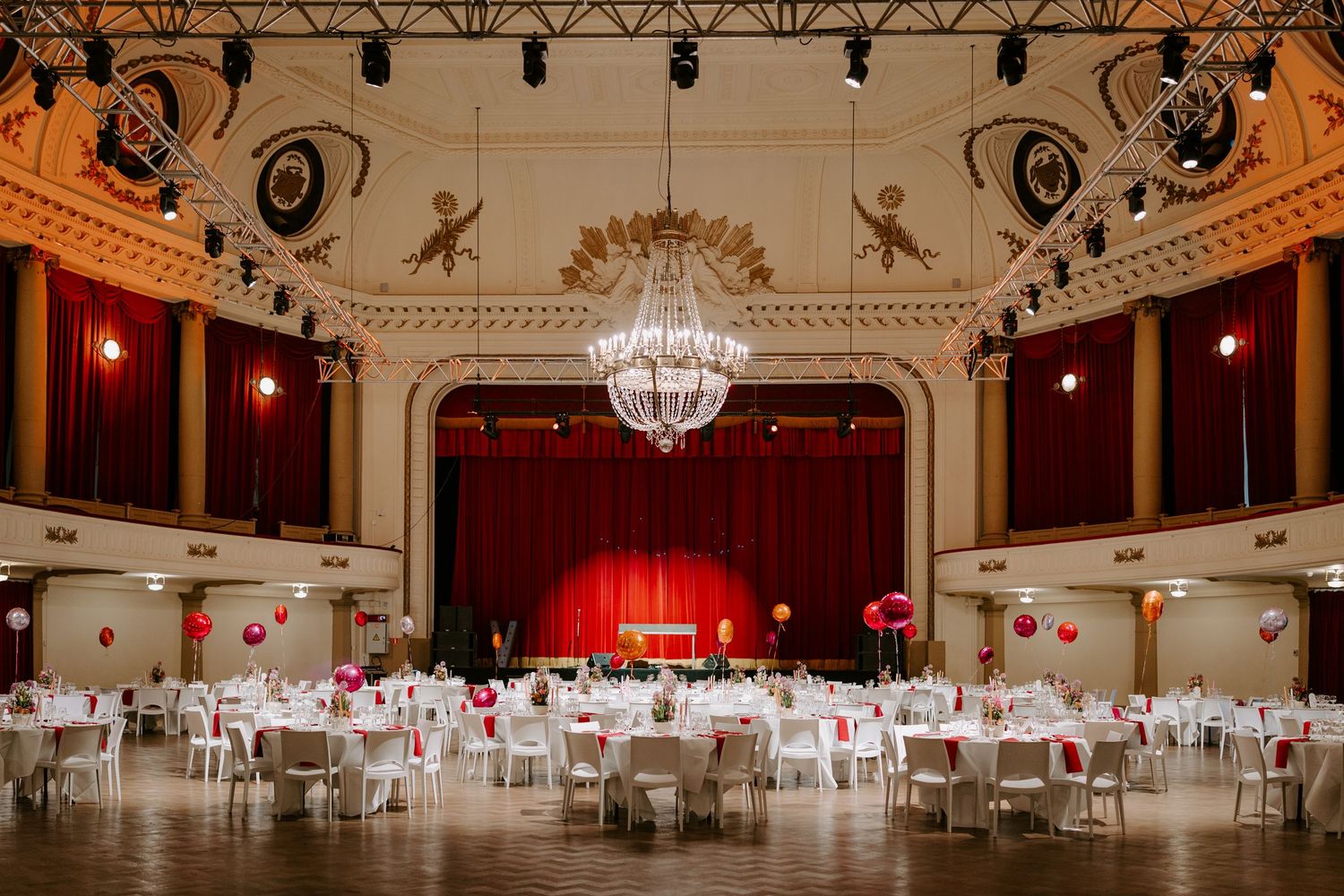 Elegant ballroom with round white tables set for gala dinner under crystal chandelier.