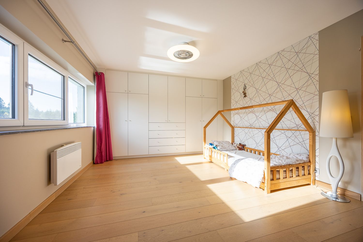 Bright children's bedroom with house-shaped wooden bed, built-in wardrobes, and geometric wallpaper.