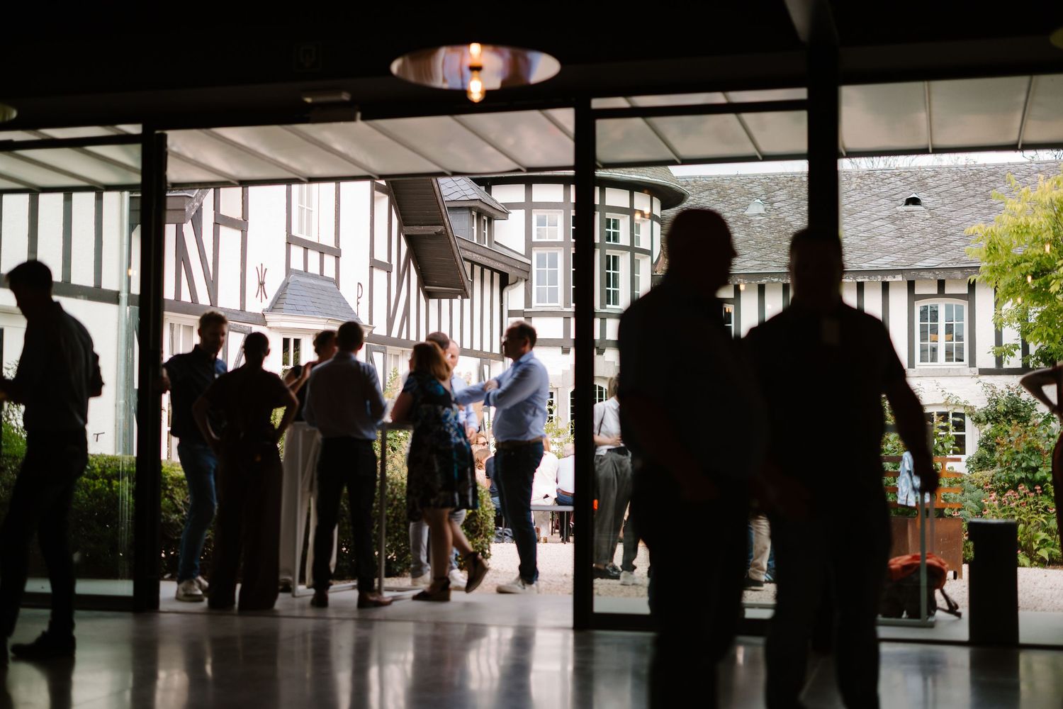 Silhouettes of people gathered at a modern venue entrance with a Tudor-style building visible outside.