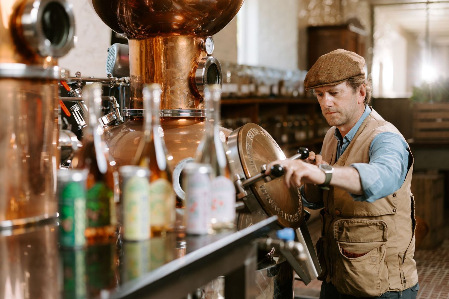 Skilled distiller working with traditional copper pot stills in a rustic artisan distillery setting.