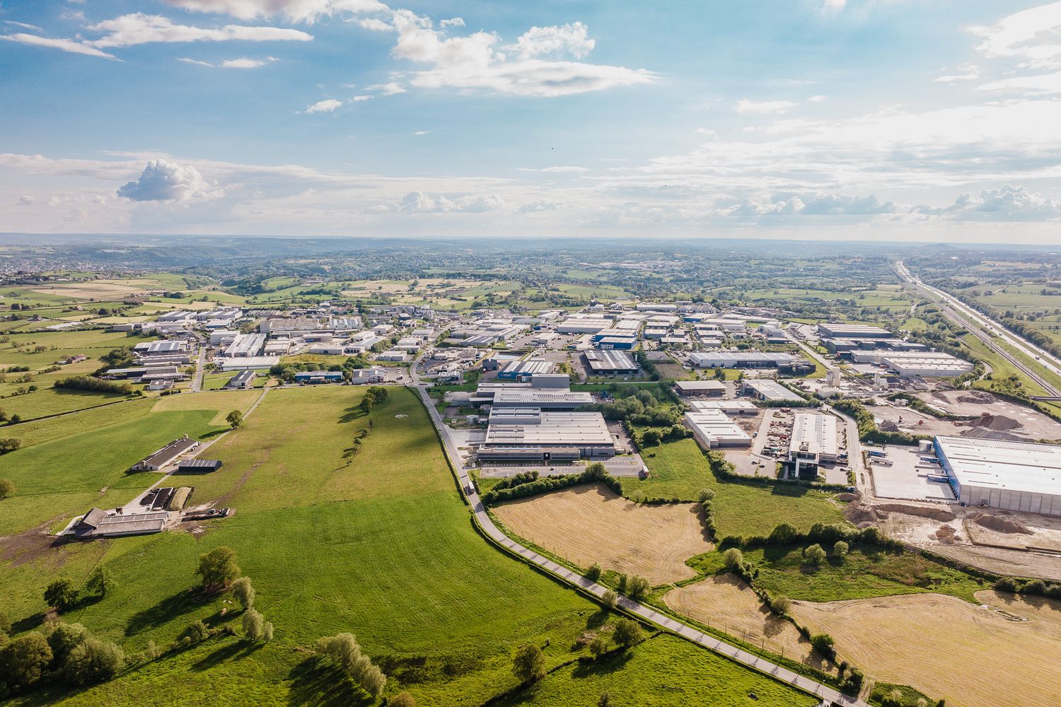Aerial view of industrial business park surrounded by green fields under blue sky.