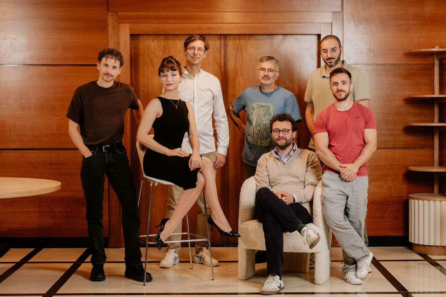 Group of seven creative professionals posing together in a stylish wood-paneled room for a team photo.