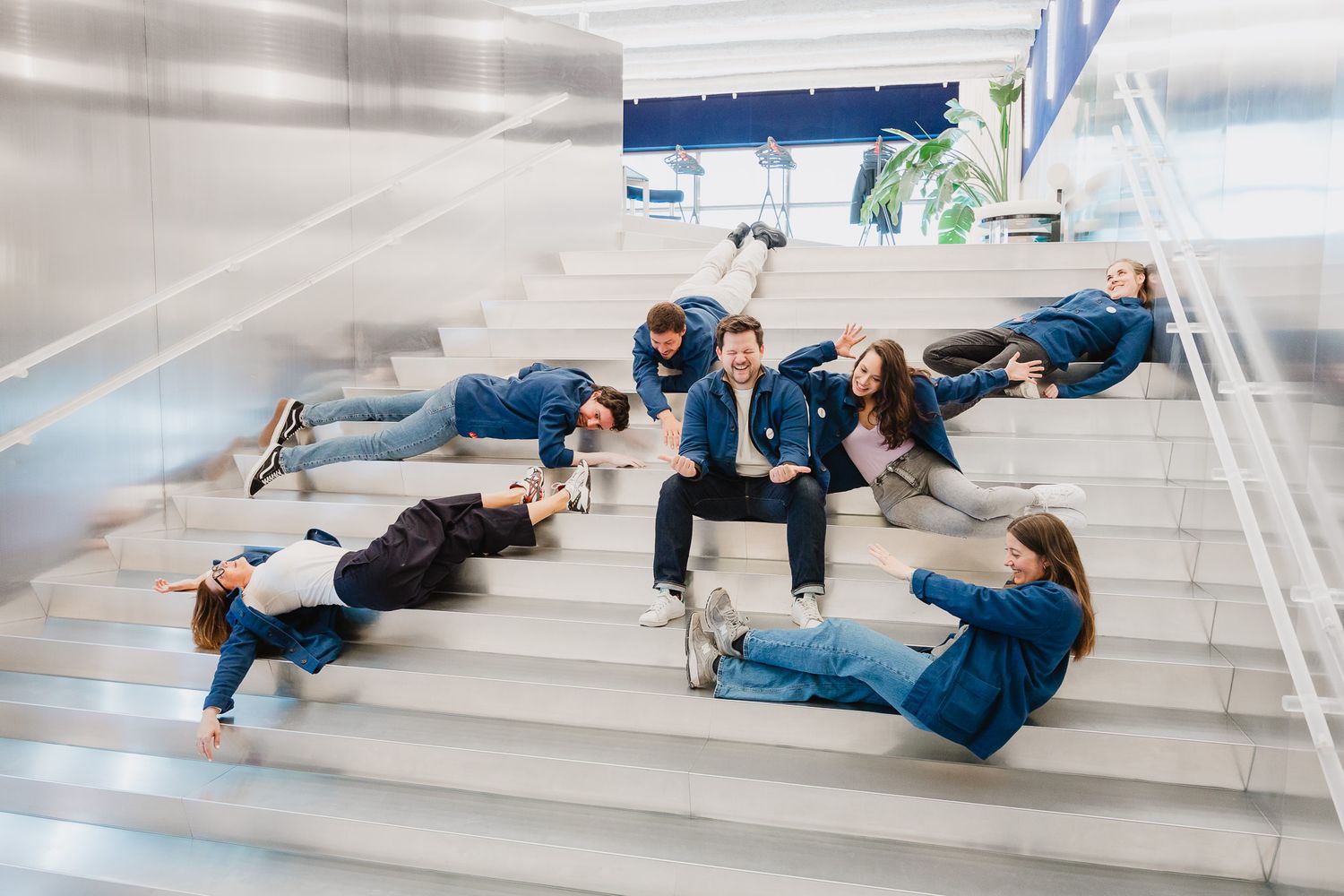 Group of young adults in denim lounging on modern white stairs, laughing and socializing in a bright indoor space.