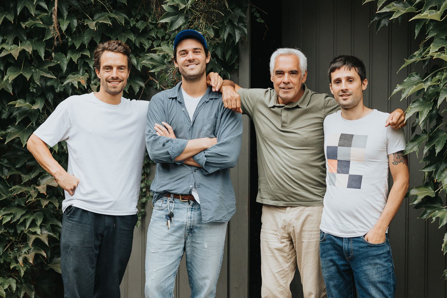 Four men smiling and posing together outdoors in front of ivy-covered wall.