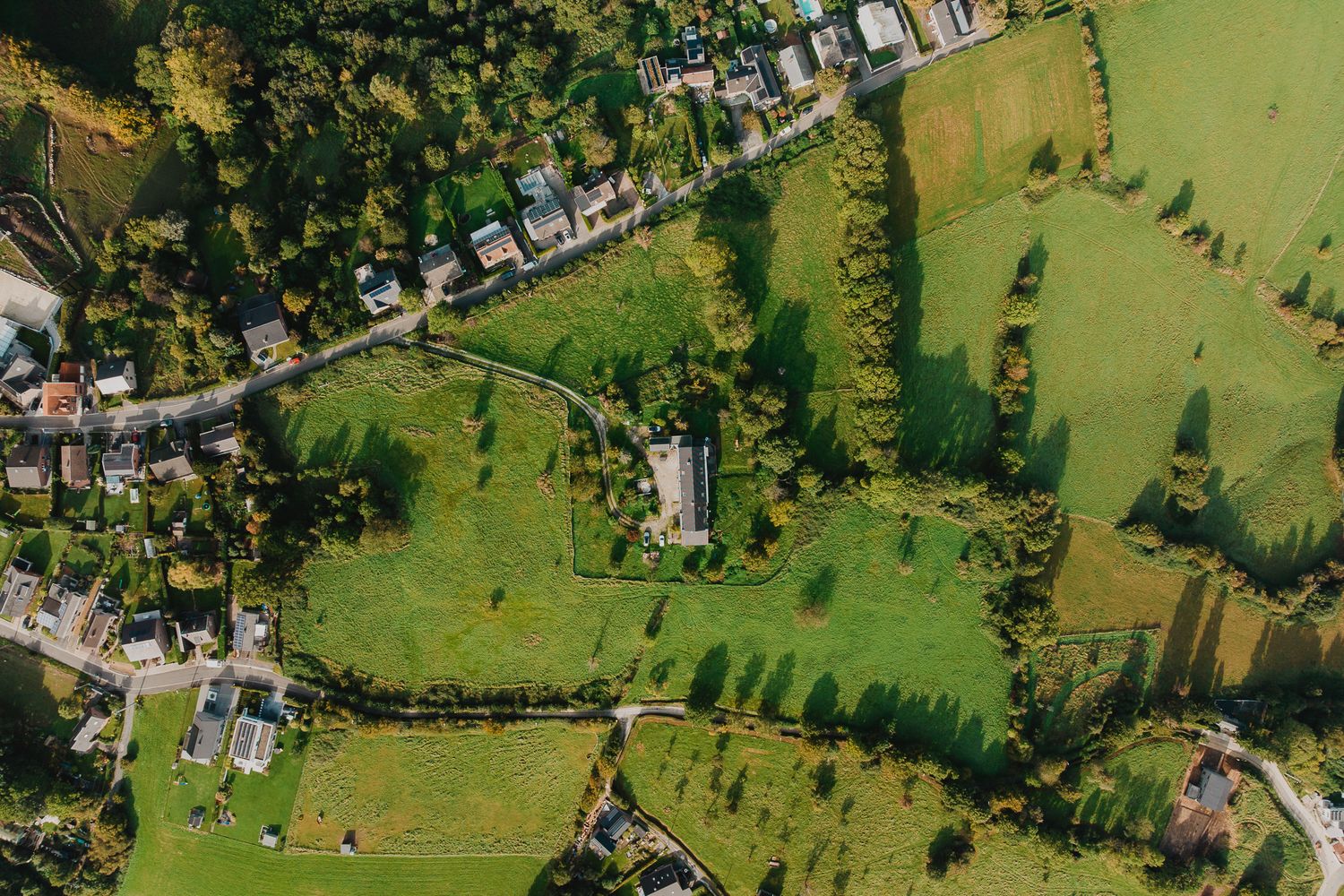 Aerial view of lush green countryside with winding path, gardens, and residential properties.