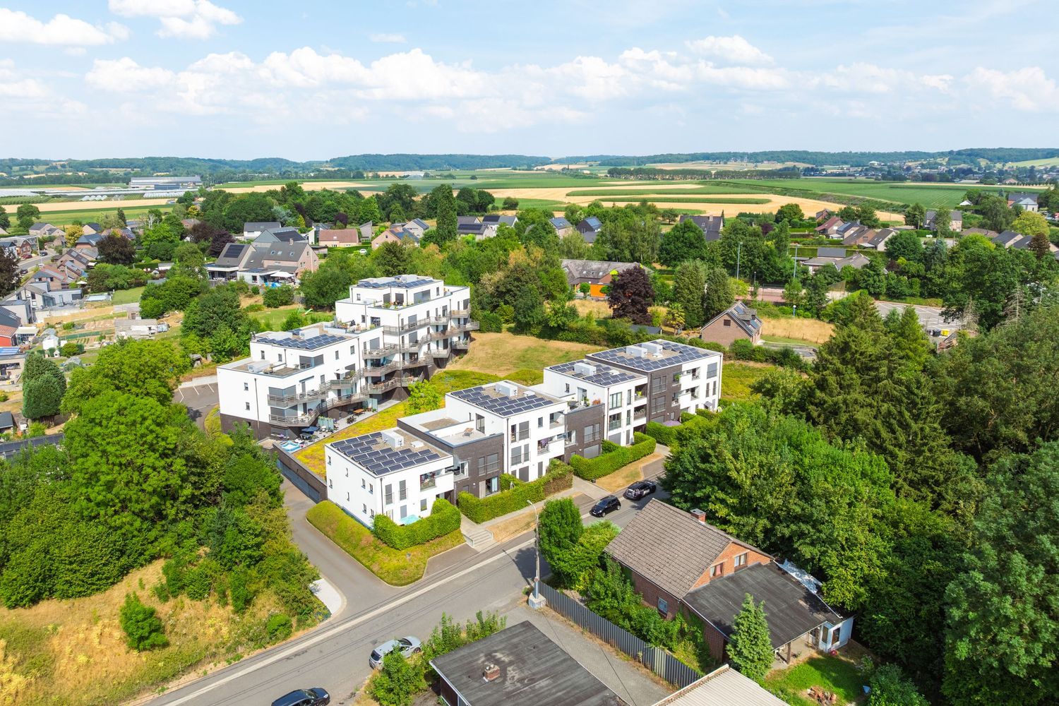Aerial view of modern white apartment buildings surrounded by lush green trees in a suburban neighborhood.