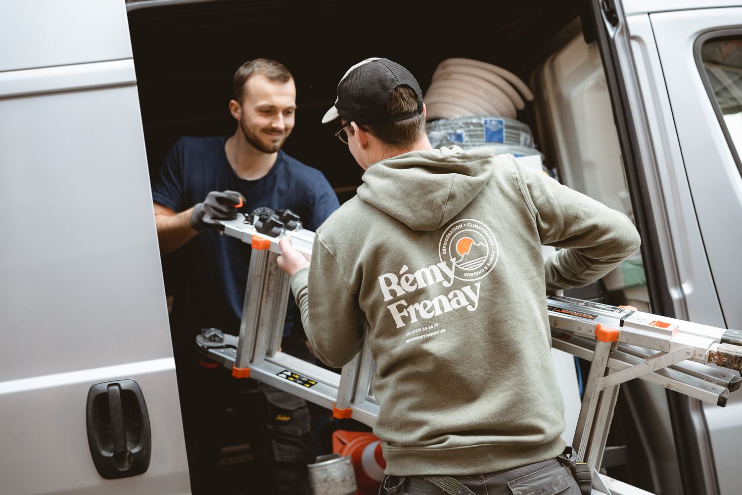 Two workers in Remy Frenay uniforms unloading equipment and ladder from a work van.