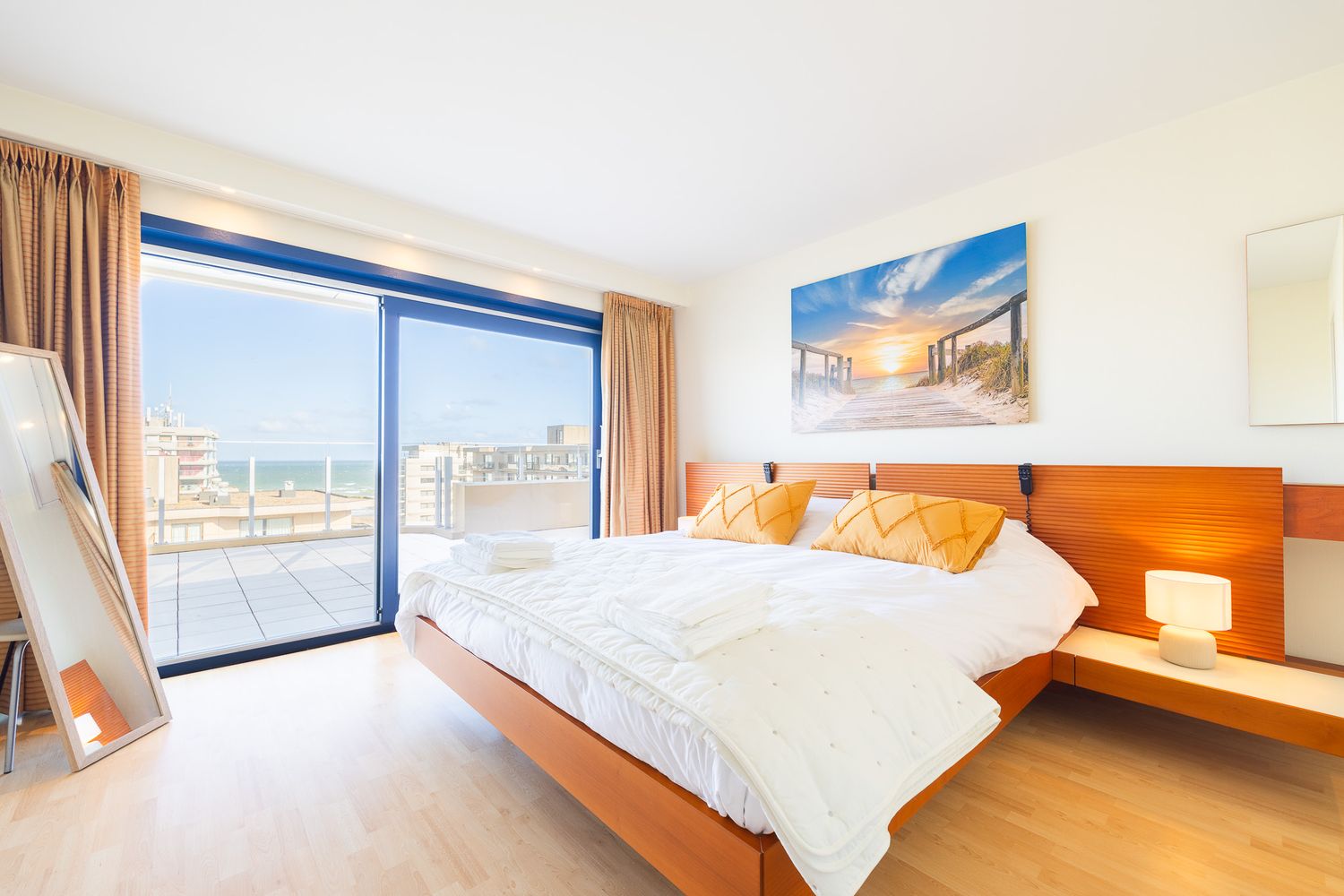 Bright bedroom with orange wood headboard, large balcony doors, and panoramic sea view.