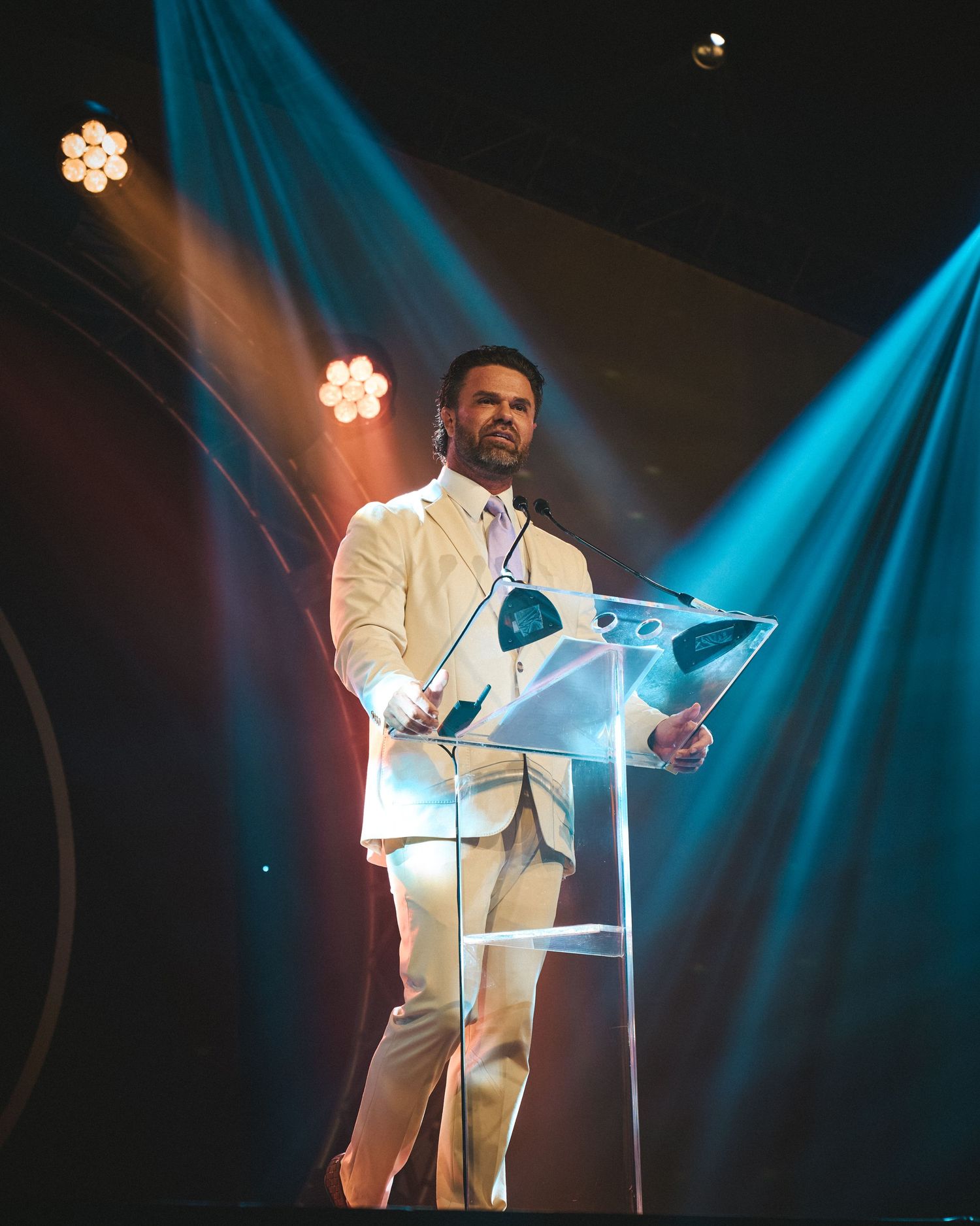 Event host speaking from the podium under bright stage lights at an awards ceremony.