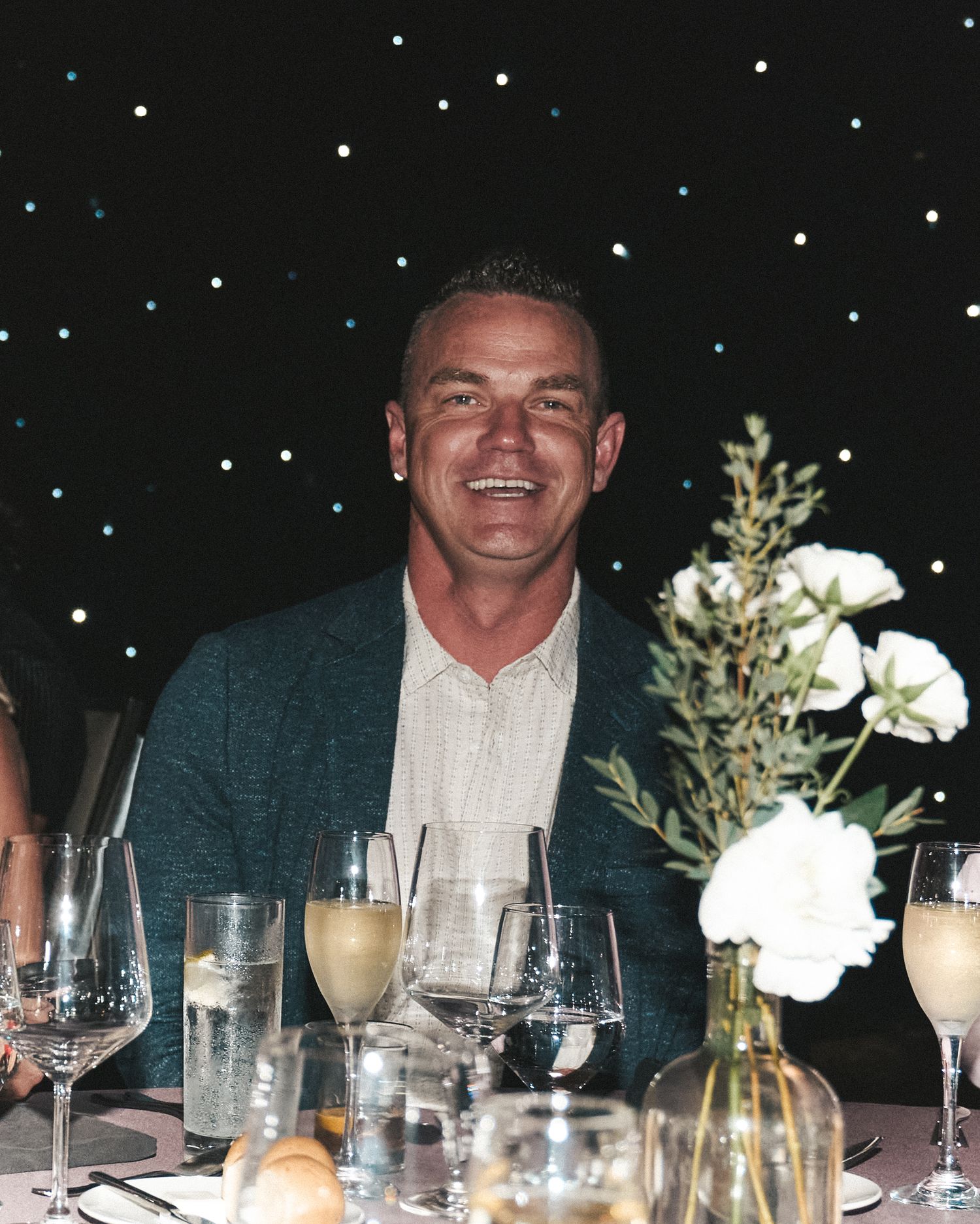 Guest smiling at the camera while seated at a gala table with a starry style backdrop behind him.