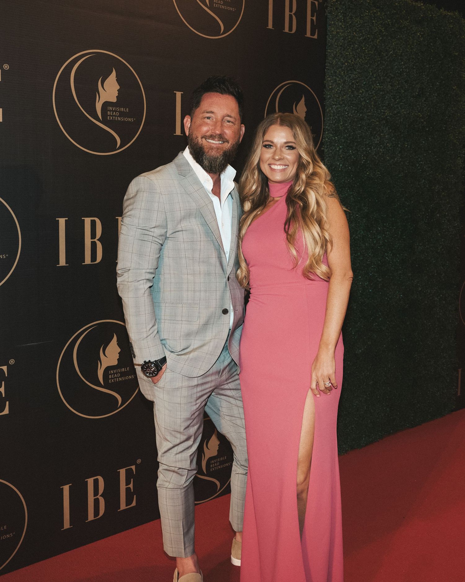 Couple smiling at the camera on the red carpet, dressed for an upscale celebration.