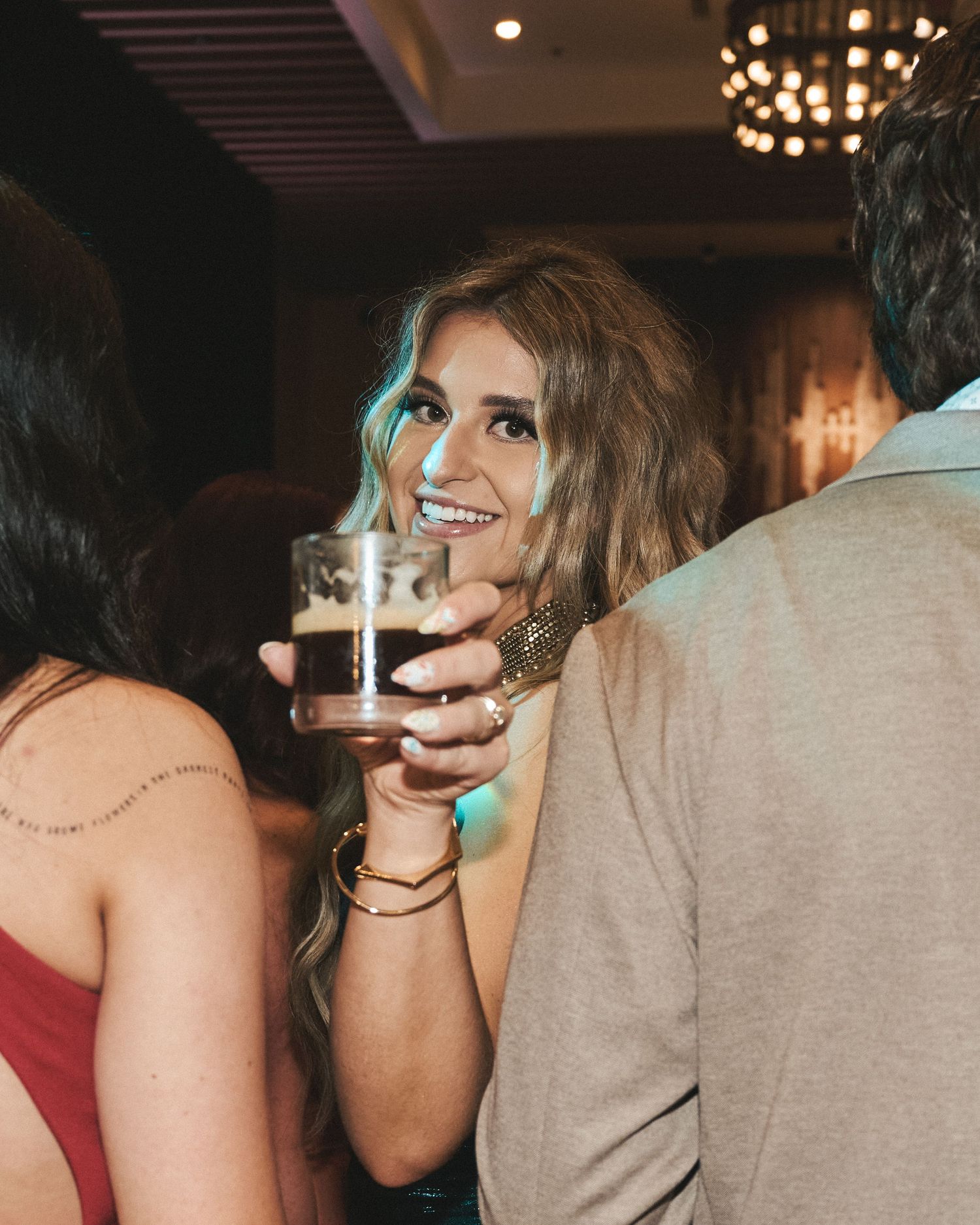 Candid shot of a guest with a drink, looking toward the camera through the crowd at a red carpet reception.