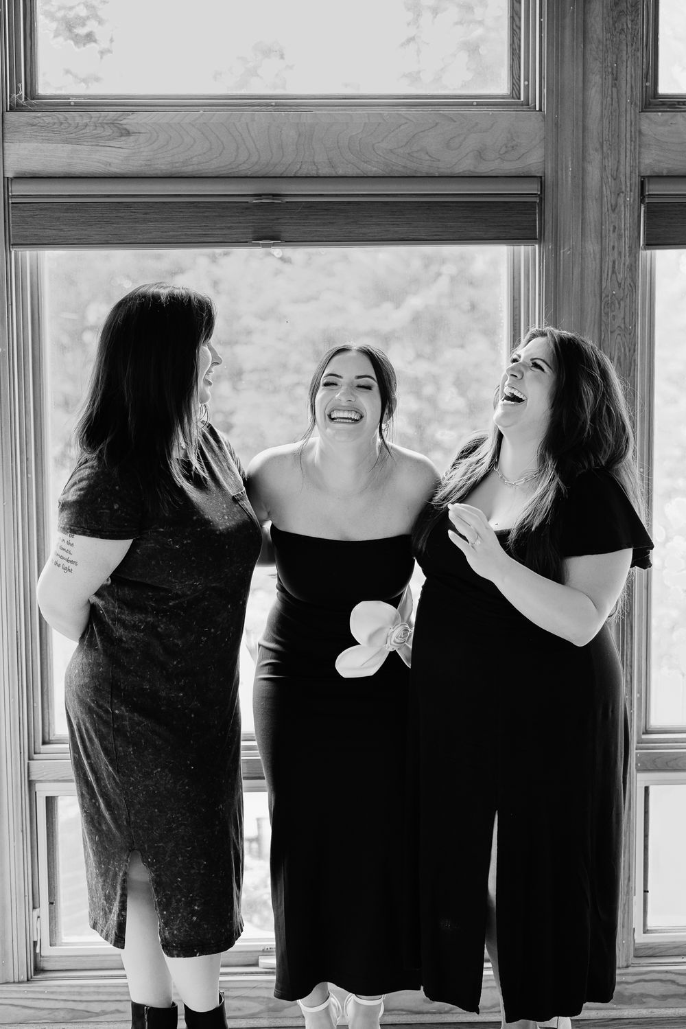 Timeless lifestyle photo session in St Charles County; Three women in black dresses sharing a laugh together by a window in black and white.
