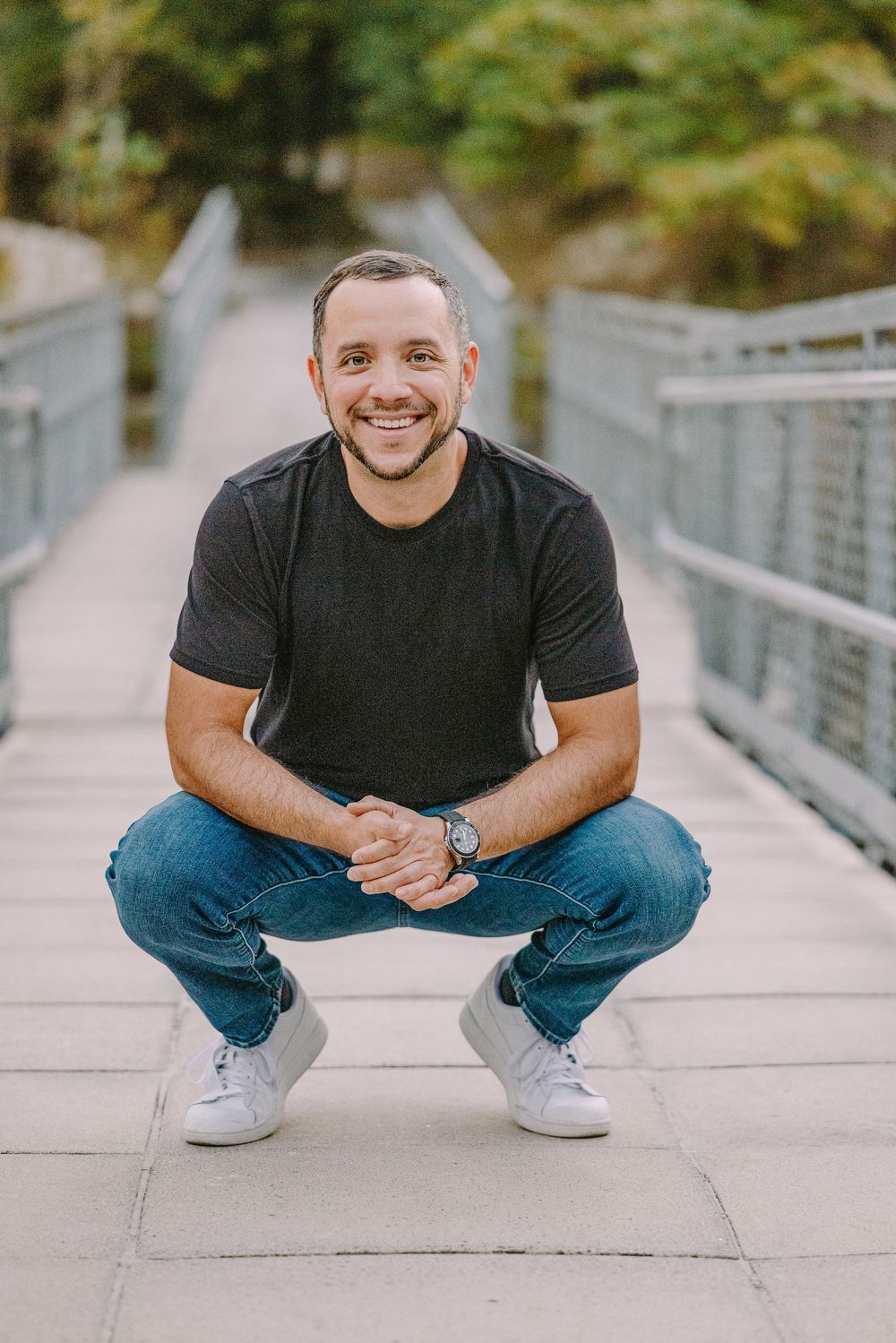 Lifestyle photo session on bridge with Casual portrait of a person squatting on a walkway wearing jeans and a black t-shirt. Klondike Park.