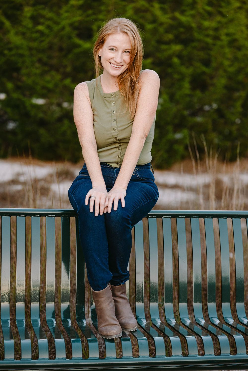Headshot photography in St Charles County Klondike park. Woman in casual attire sitting on park bench with green foliage backdrop.