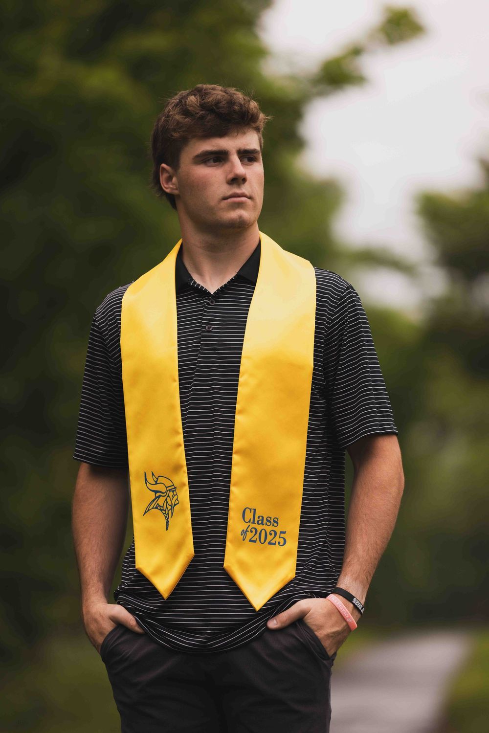 Graduate wearing a yellow Class of 2025 stole and striped shirt outdoors.