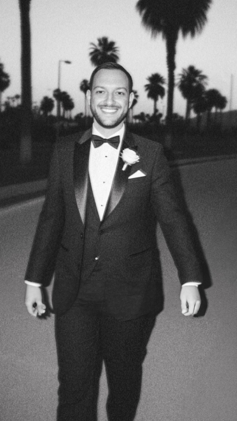 Cinematic moment captured in timeless black A black and white portrait of a person in a tuxedo standing on a palm tree-lined street. OFallon