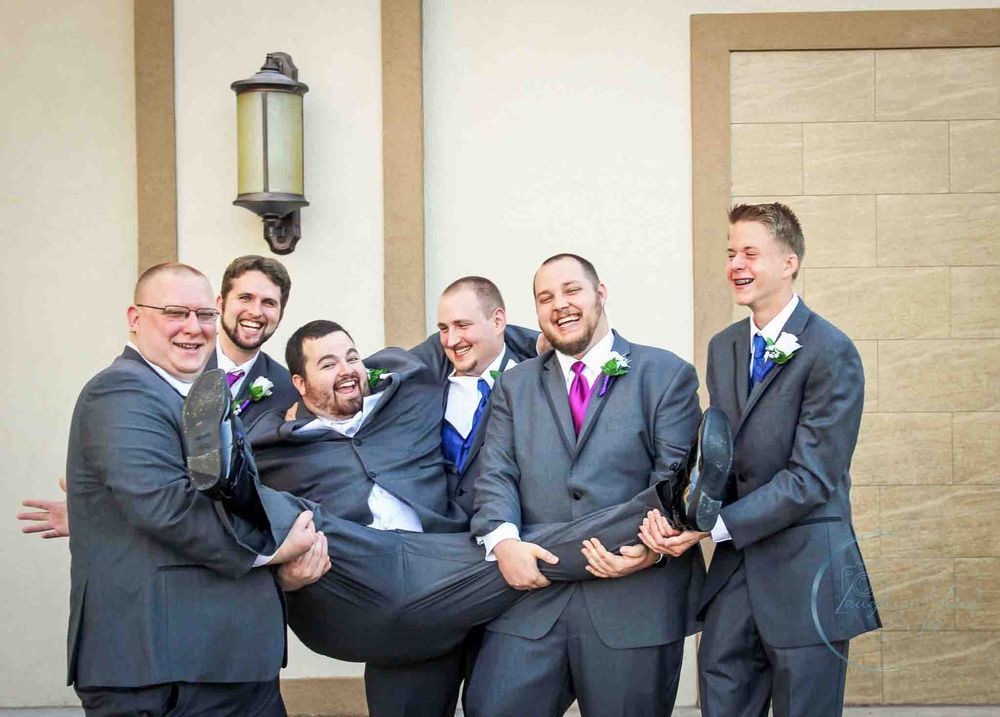 Wedding portrait in Saint Charles County of groomsmen in gray suits and colorful ties laugh together while posing outside a building.