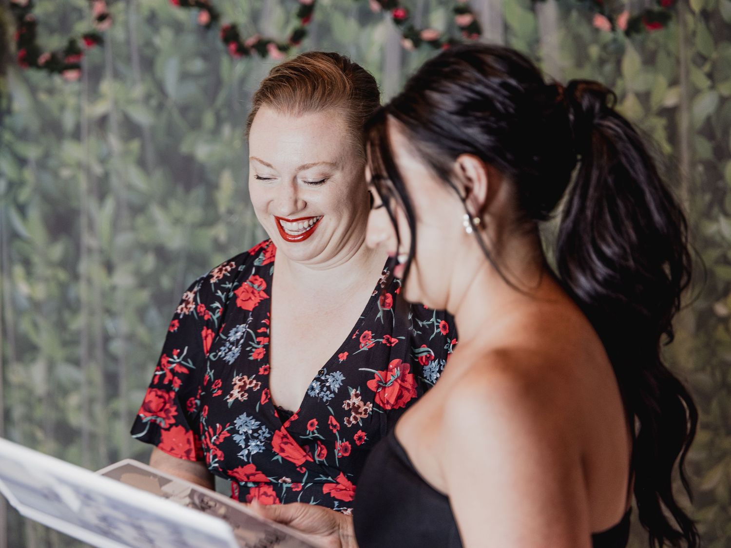Two people share a joyful moment while looking at something together against a floral backdrop.