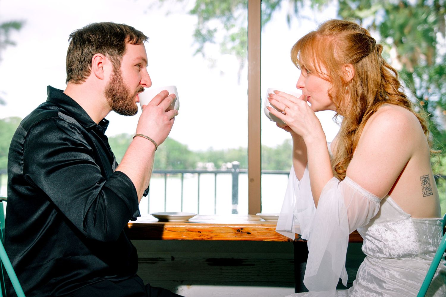 A couple shares an intimate moment drinking coffee together at a table near a scenic waterfront view.