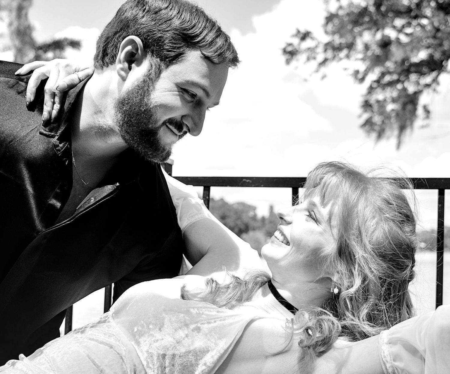 Black and white photo of a smiling couple sharing a romantic moment on a balcony.