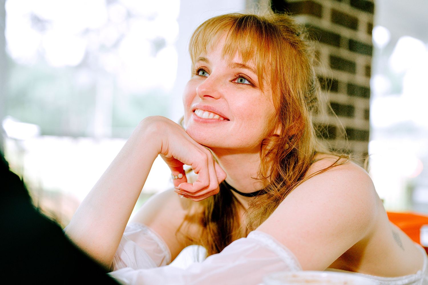 Beautiful smiling woman with long red hair resting her chin on her hand in a bright cafe.