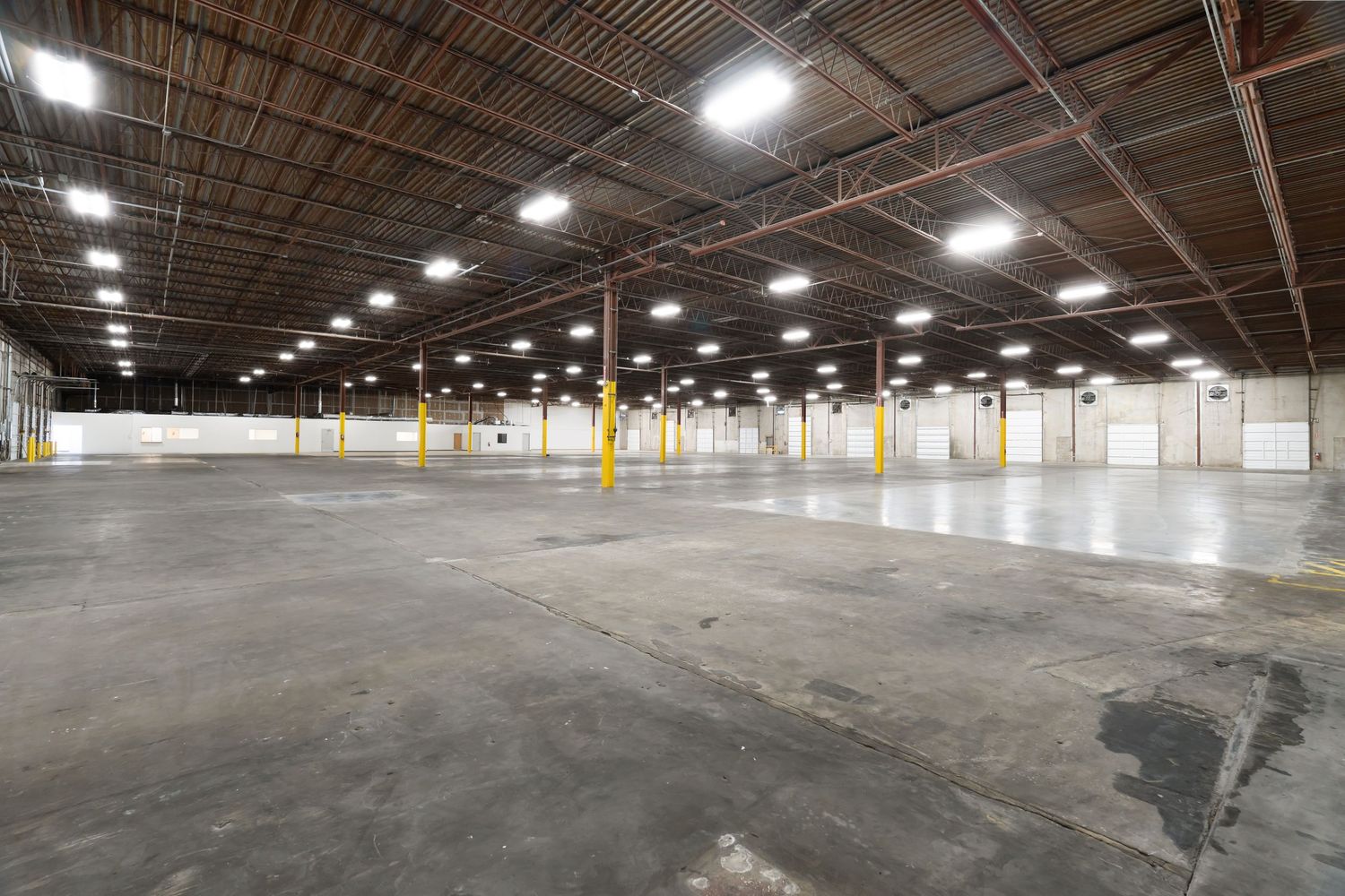 Large empty industrial warehouse interior with concrete floors and bright overhead lighting showing multiple connected spaces.